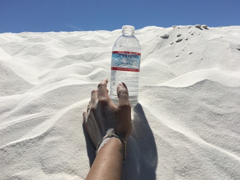 A close-up of an athlete’s hands holding a sleek hydration bottle against a warm sand background.