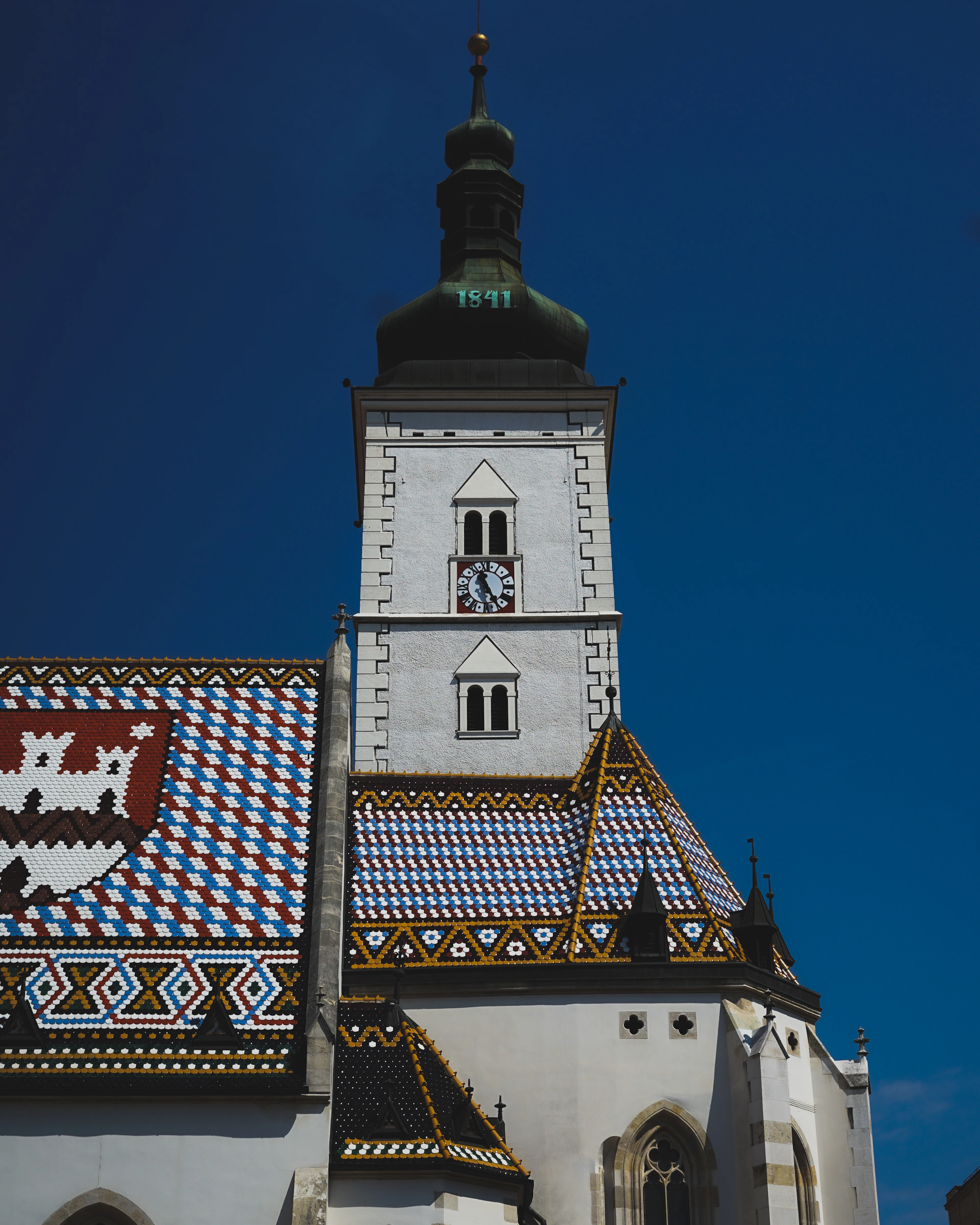 Close-up of St. Mark's Church roof in Zagreb, its colourful tiles forming the Croatian and Zagreb coats of arms against deep blue sky.