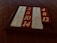 A sliding puzzle consisting of numbered tiles arranged in a 4x4 grid with one missing tile. The tiles are alternately colored red and white, and are encased in a dark brown frame. The numbers are embossed in a gold color.