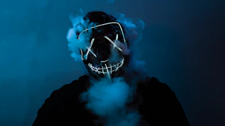 Close-up of a neon green glowing samurai mask printed on a black t-shirt with smoky background.