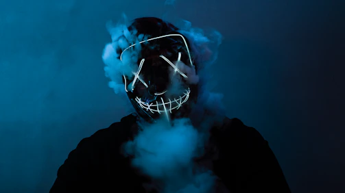 Close-up of a neon green glowing samurai mask printed on a black t-shirt with smoky background.