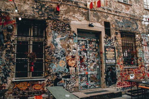 A vibrant urban street wall covered in colorful, neon green and red graffiti-style stickers and posters.