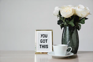 white flowers, coffee mug & a motivational picture on a desk