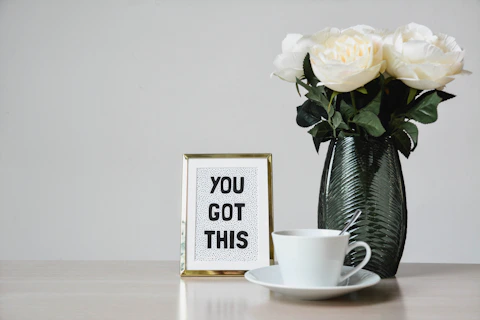 white flowers, coffee mug & a motivational picture on a desk