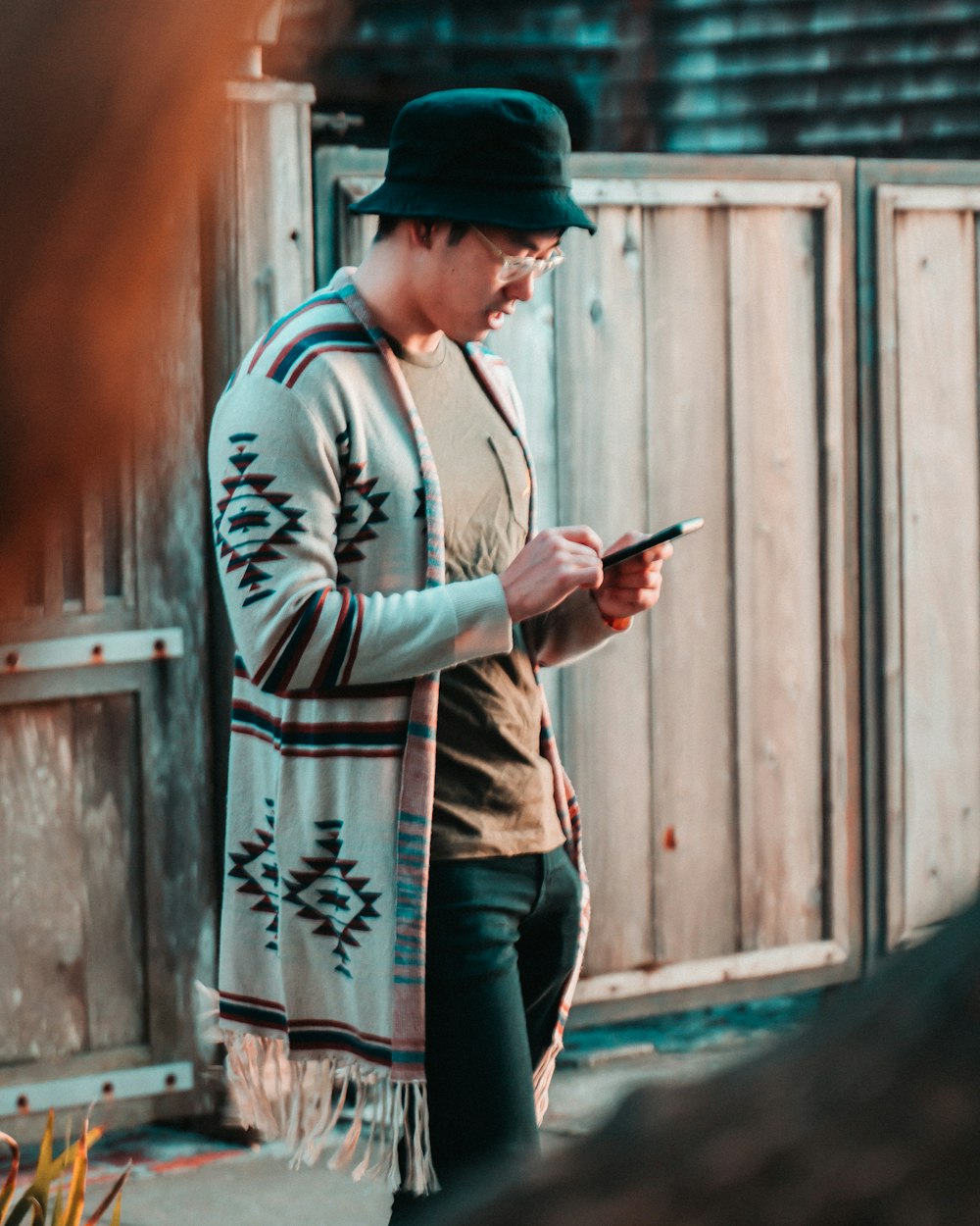 man standing near wooden gate browsing smartphone