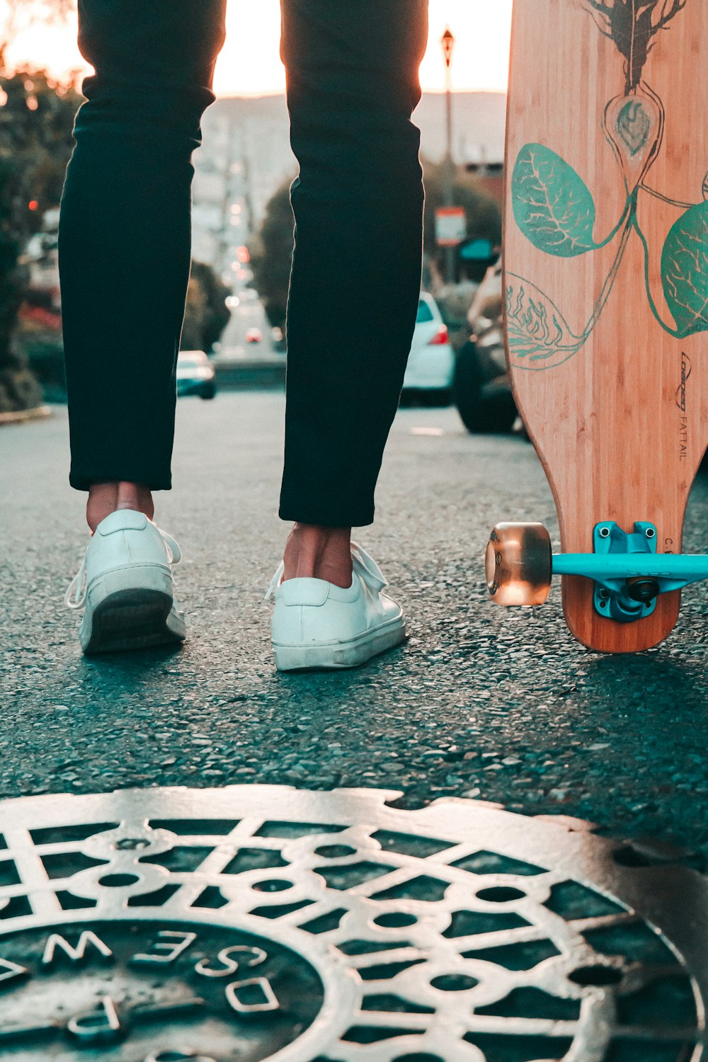 person wearing black jeans and white low-top sneaker standing near brown skateboard