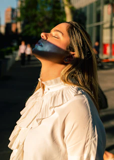 Smiling woman with flawless skin basking in warm sunlight outdoors.