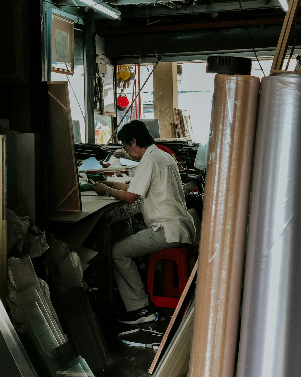 man using phone while sitting on red plastic stool near table