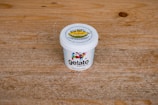 A white ice cream container with the label 'gelato more than life', featuring colorful designs and a lid that mentions 'Kungfu Durian'. The container is placed on a textured wooden surface.