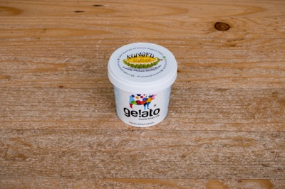 A white ice cream container with the label 'gelato more than life', featuring colorful designs and a lid that mentions 'Kungfu Durian'. The container is placed on a textured wooden surface.