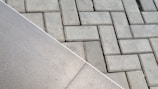 The image displays two different types of surfaces divided diagonally. The left side shows a smooth, possibly ceramic or concrete tile surface. The right side features a pattern of interlocking grey concrete bricks with a herringbone layout.