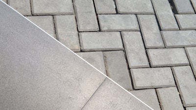 The image displays two different types of surfaces divided diagonally. The left side shows a smooth, possibly ceramic or concrete tile surface. The right side features a pattern of interlocking grey concrete bricks with a herringbone layout.