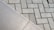 The image displays two different types of surfaces divided diagonally. The left side shows a smooth, possibly ceramic or concrete tile surface. The right side features a pattern of interlocking grey concrete bricks with a herringbone layout.
