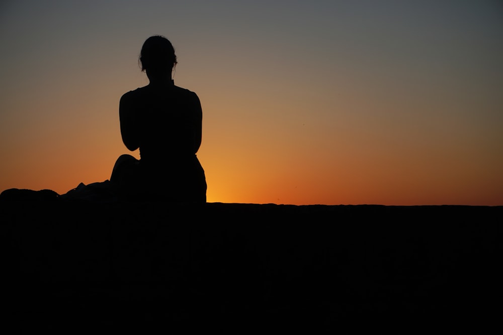 a silhouette of a person sitting on a rock at sunset