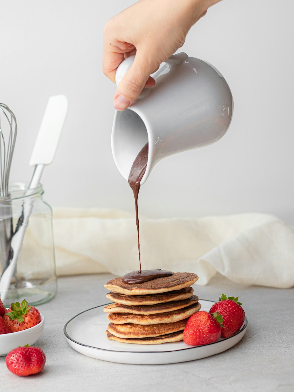 man pouring maple syrup on piled of pancake