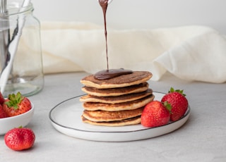 man pouring maple syrup on piled of pancake