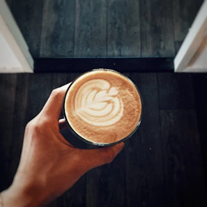 Close-up of a hand holding a steaming cup of laraco coffee with golden light reflecting off the dark brown mug.