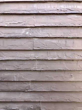 Close-up of a painter carefully applying oil-based primer on weathered cedar siding.