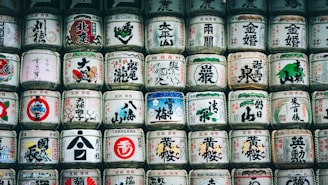 A collection of traditional Japanese sake barrels stacked in rows, each adorned with vibrant kanji characters and symbolic illustrations. The barrels are made of straw and cloth, presenting a harmonious blend of colors and patterns that reflect Japanese cultural motifs.
