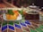 A glass teapot filled with herbal tea is placed on a patterned table alongside a white plate containing slices of cake garnished with fresh mint leaves.