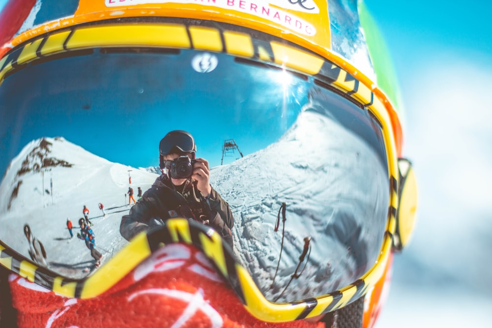 reflection of man holding camera on person's goggles