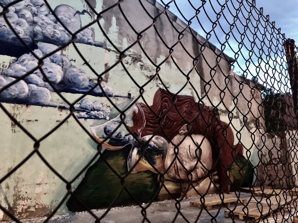 a painting on the side of a building behind a chain link fence