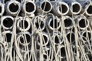 A stack of cylindrical concrete pipes with ropes intertwined around them. The pipes appear weathered and are arranged in a dense, repetitive pattern.