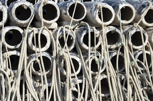 A stack of cylindrical concrete pipes with ropes intertwined around them. The pipes appear weathered and are arranged in a dense, repetitive pattern.
