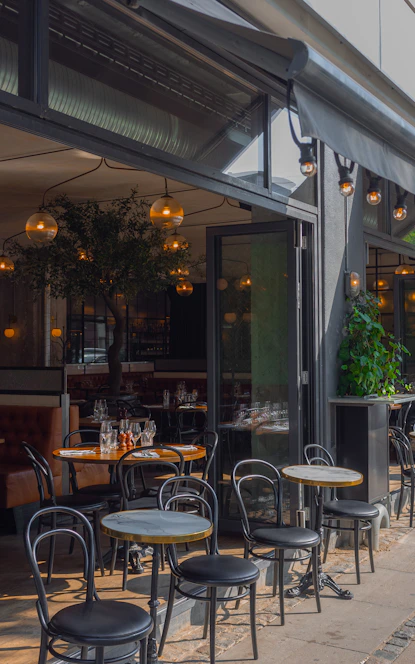 Tables and chairs on a restaurant patio with an open glass storefront