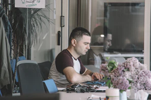 A translator at a desk surrounded by funeral and vital records, gently working on a laptop.