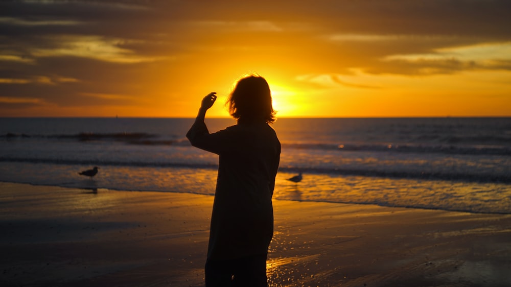 silhouette of woman standing on seashore during sunset