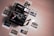 A vintage Polaroid camera is surrounded by several instant photographs depicting various outdoor scenes such as buildings, a bridge, and a landscape, all placed on a light wooden surface. The camera is the focal point, with a colorful stripe decal, and the photos appear slightly scattered.