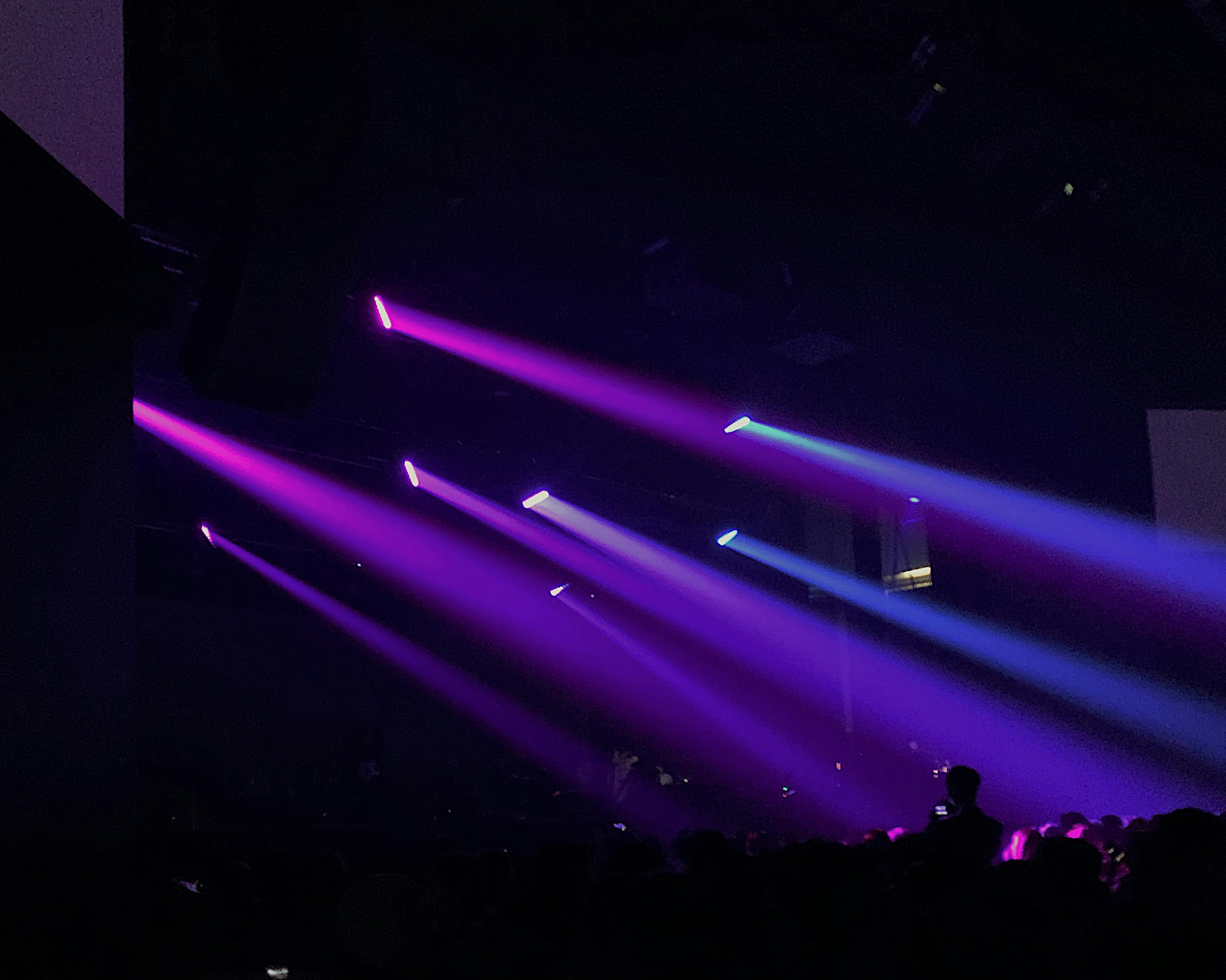 Dark concert stage with electric blue and purple lights, deep black background, intense atmosphere