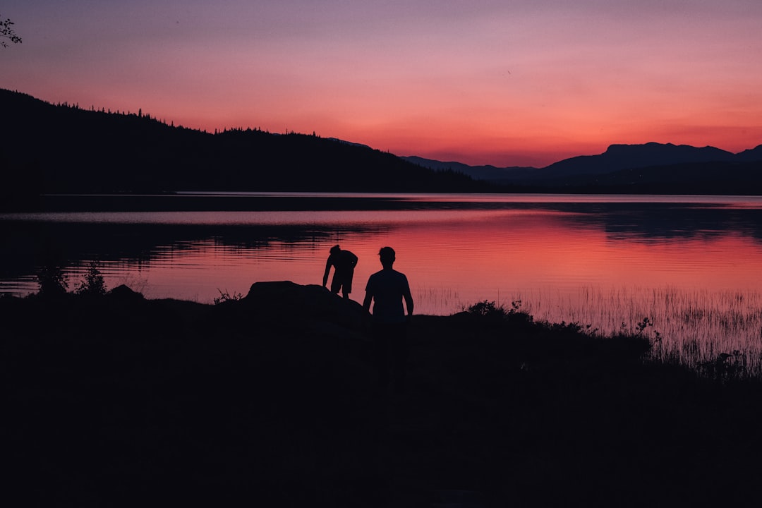 silhouette of two people standing near body of water under orange sky