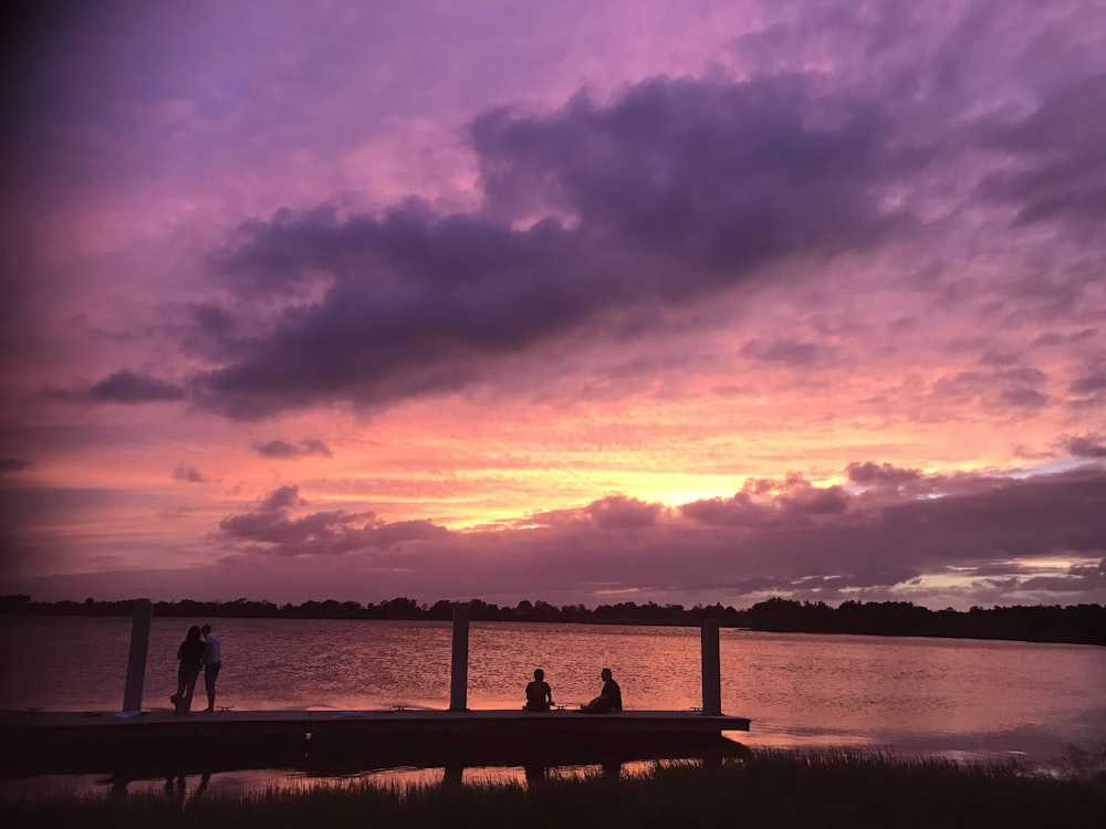 a group of people sitting on a dock watching the sunset