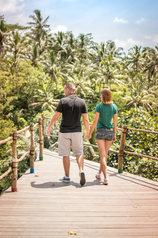 The couple holding hands on a rustic wooden bridge framed by lush greenery.