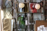 Several rectangular and diamond-shaped mirrors are displayed, hanging on a rustic wooden backdrop. Reflections include string lights and a person in a red coat. Some price tags are visible, and a few white cylindrical objects are in the foreground.