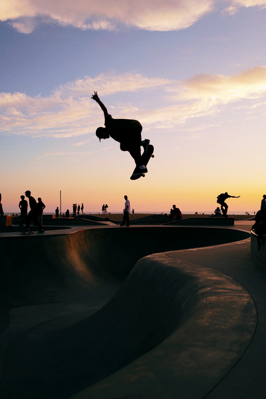 A skateboarder silhouetted mid-air above a bowl at sunset