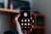 A hand holds a smartphone displaying a screen where various cartoon emoji faces are featured. The background is softly blurred, indicating an indoor setting with possibly a shelf or furniture.