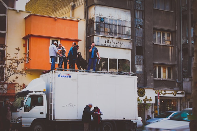 A delivery truck parked near a film set with crew members unloading equipment.