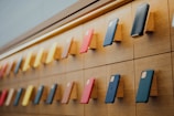 A well-organized display of mobile phones mounted on a wooden wall with various colored cases, arranged in rows with a sleek and modern lighting design accentuating the layout.