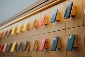 A well-organized display of mobile phones mounted on a wooden wall with various colored cases, arranged in rows with a sleek and modern lighting design accentuating the layout.