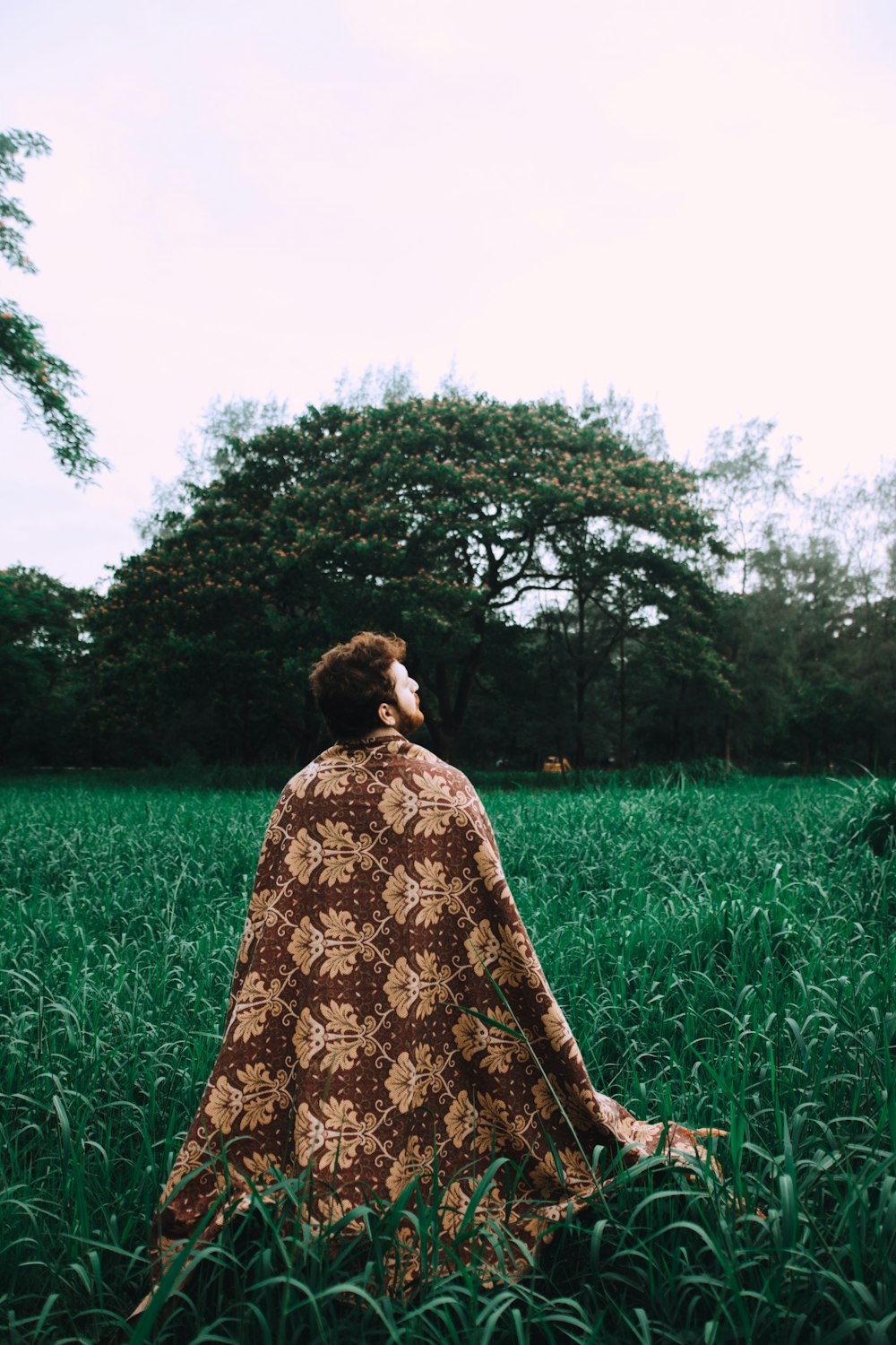 man wearing brown floral robe surrounded by grass