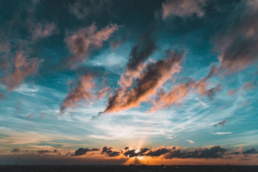 the sun is setting over the ocean with clouds in the sky