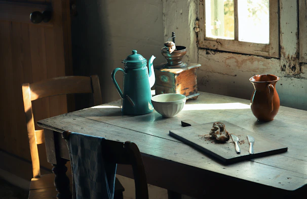 A rustic wooden table set with a steaming mug, a linen apron, and vintage bakery utensils bathed in soft morning light.