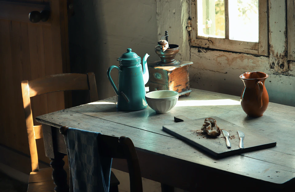 A rustic kitchen table with jars of desi ghee, mustard oil, and fresh pulses arranged alongside a sack of flour, bathed in warm natural light.