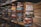 Stacks of paperback books are arranged on wooden shelves in a somewhat cluttered manner. Various genres and titles are visible, featuring works by authors such as John Sandford and W.E.B. Griffin. The scene conveys a sense of an extensive, varied collection typical of a well-stocked bookstore or personal library.