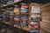 Stacks of paperback books are arranged on wooden shelves in a somewhat cluttered manner. Various genres and titles are visible, featuring works by authors such as John Sandford and W.E.B. Griffin. The scene conveys a sense of an extensive, varied collection typical of a well-stocked bookstore or personal library.