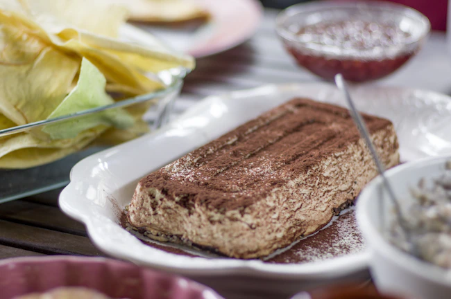 Close-up of a creamy tiramisu dusted with cocoa powder on a rustic wooden table.