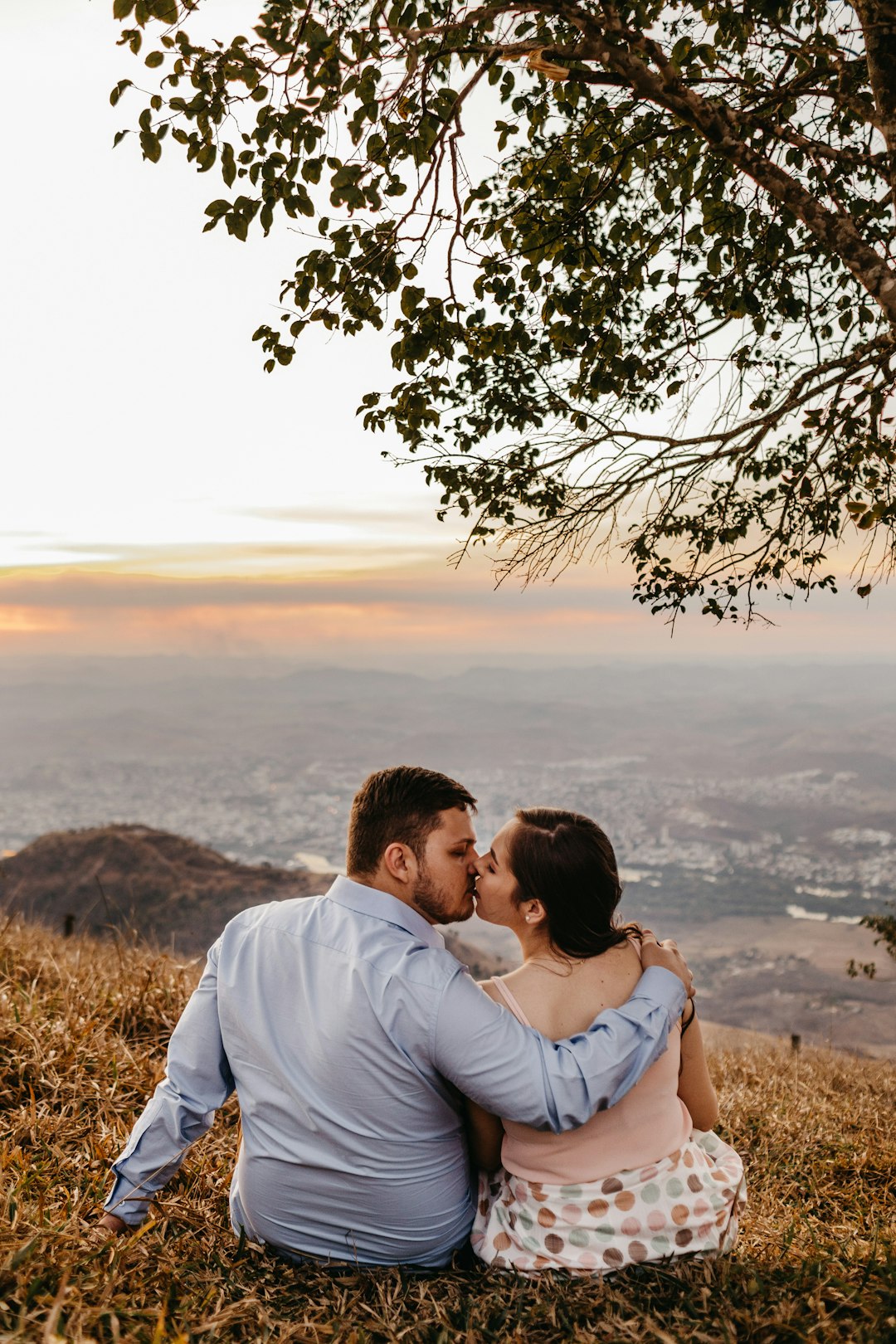 man and woman sitting on ground while kissing under the tree